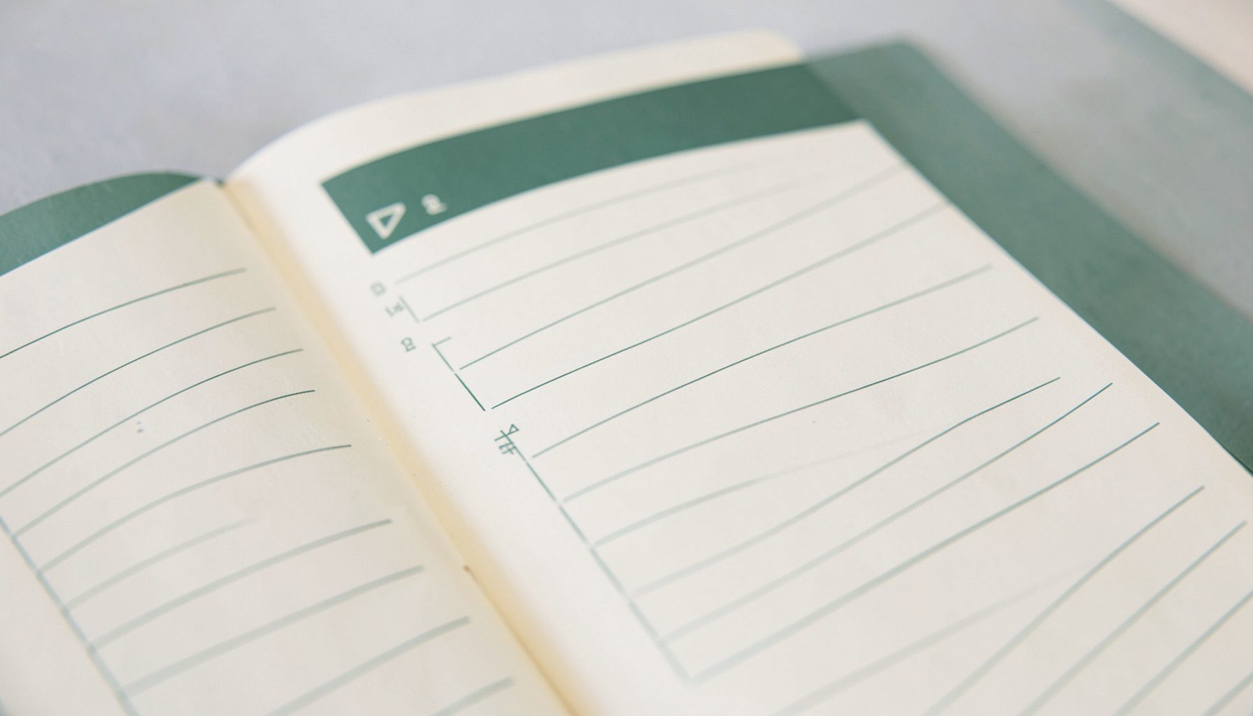 Closeup of an open daily planner page with ruled lines and a simple checklist, in soft cream and forest-green colors