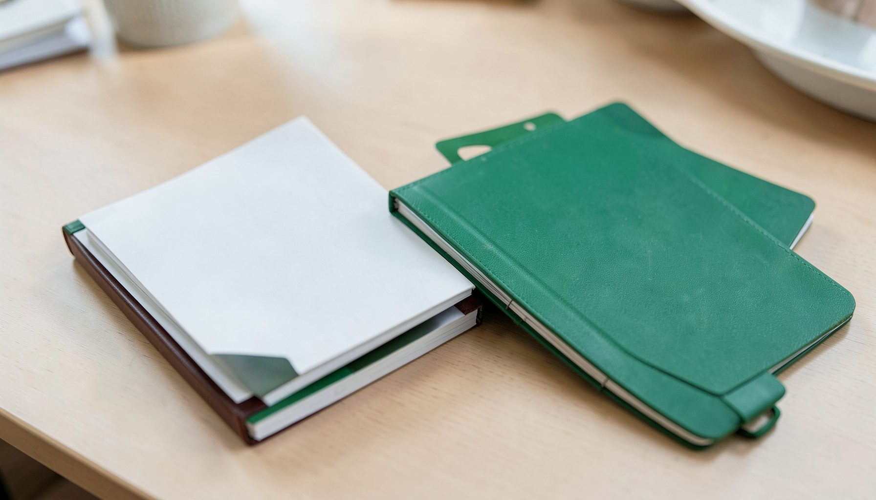 Stack of notebooks and a daily planner with green cover tones resting on a desk