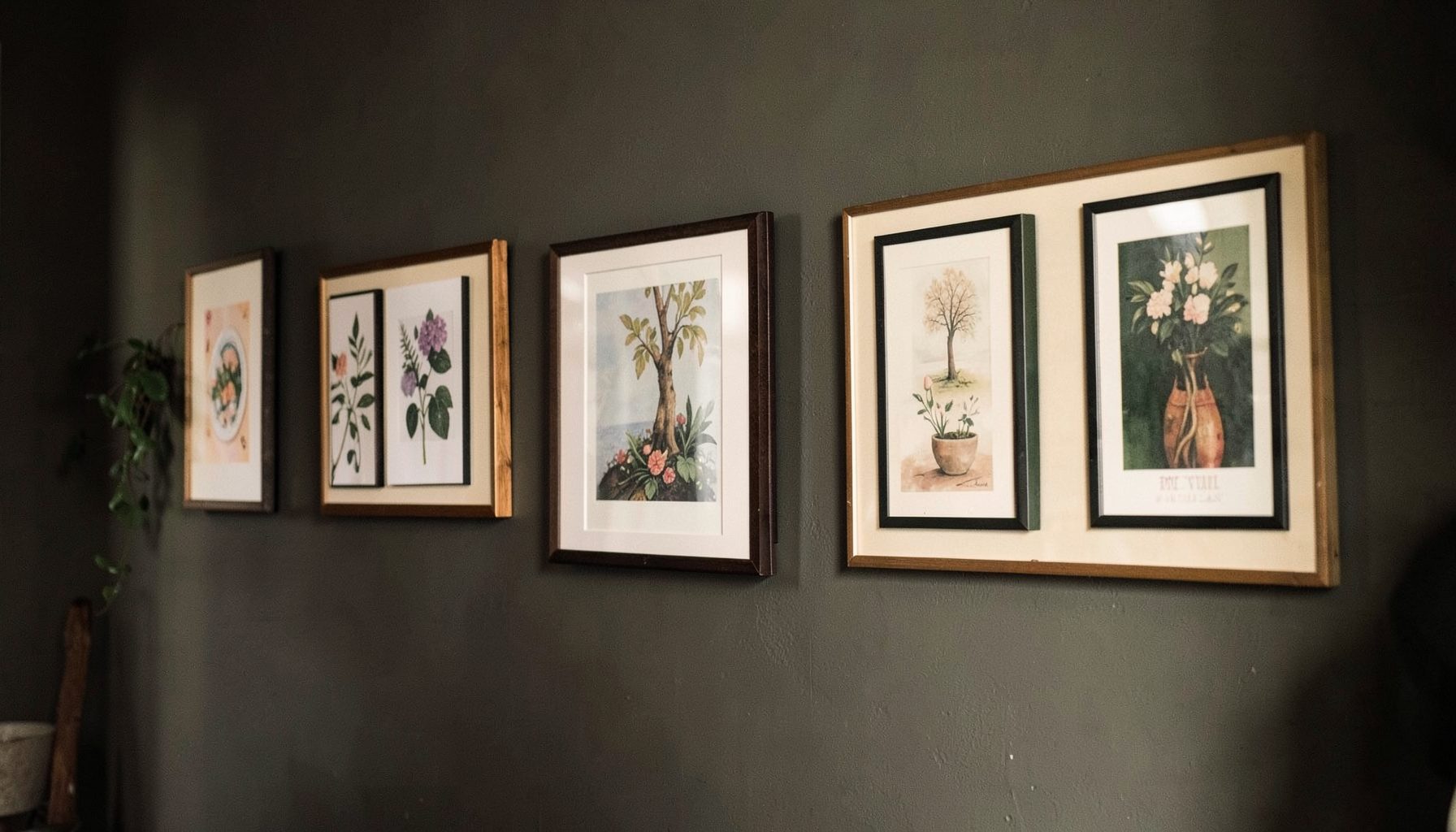 Warm charcoal-and-green toned wall display of framed art prints hanging in a row, cozy and inspirational mood